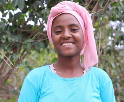 Girl from Ethiopia standing in front of a tree, looking at the camera.