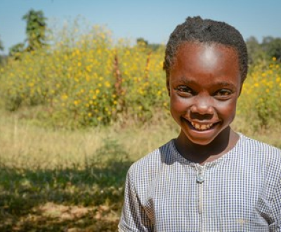 Former sponsored child smiles in field in Zambia