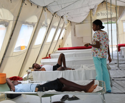 A nurse stands in the middle of a cholera tent in Haiti with patients lying on beds