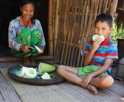 Mother from Myanmar and her son sat on the floor on their porch while eating a melon.