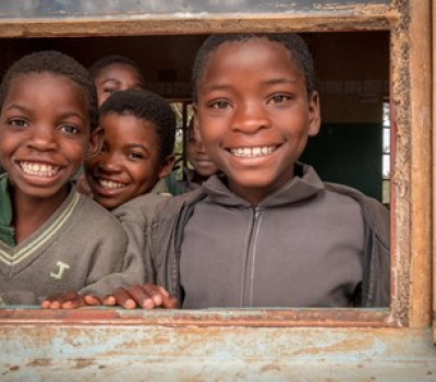 School children peering out of a window, smiling 