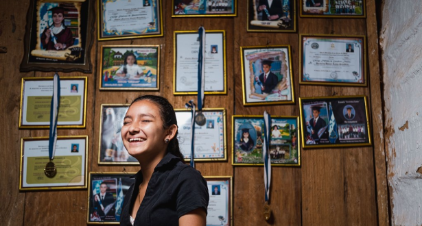 Girl from Honduras laughing while standing in front of a wall with certificates and ribbons hung on it