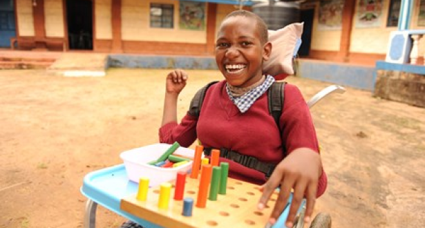 Girl from Kenya smiling while sitting in her wheelchair and playing with blocks