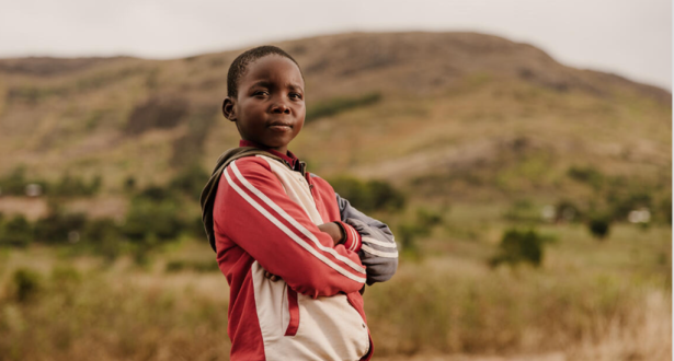 Boy from Malawi standing with his arms crossed in a field.