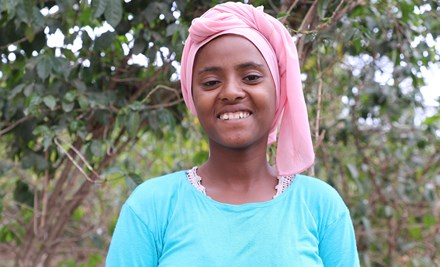 Girl from Ethiopia standing in front of a tree, looking at the camera.