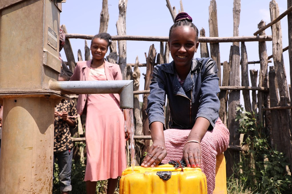 Girl from Ethiopia pours water from public tap into a yellow tub