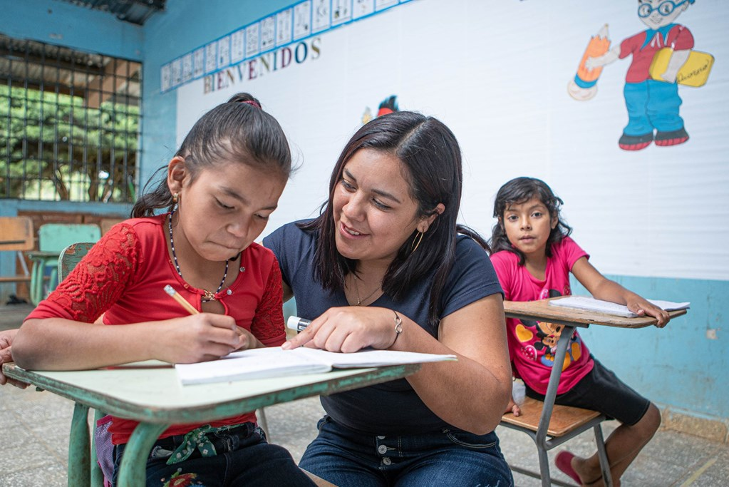 Teacher in Honduras helping a student with her work at her school desk