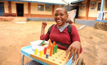 Girl from Kenya smiling while sitting in her wheelchair and playing with blocks