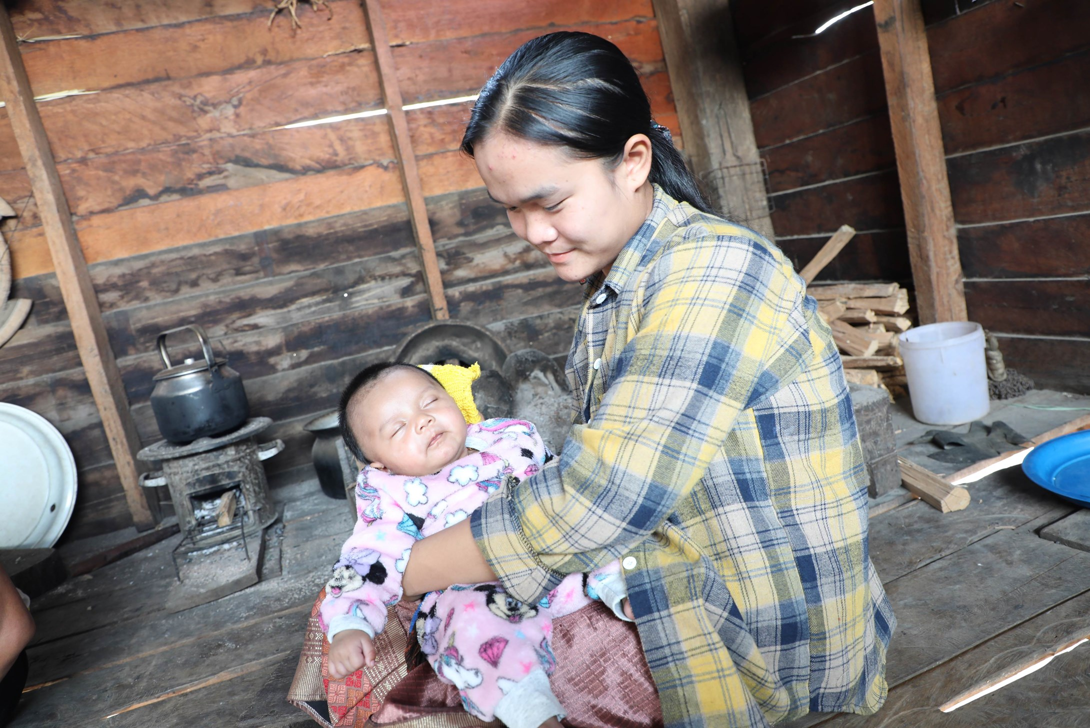 A teenage mother from Laos holding her baby in her home.