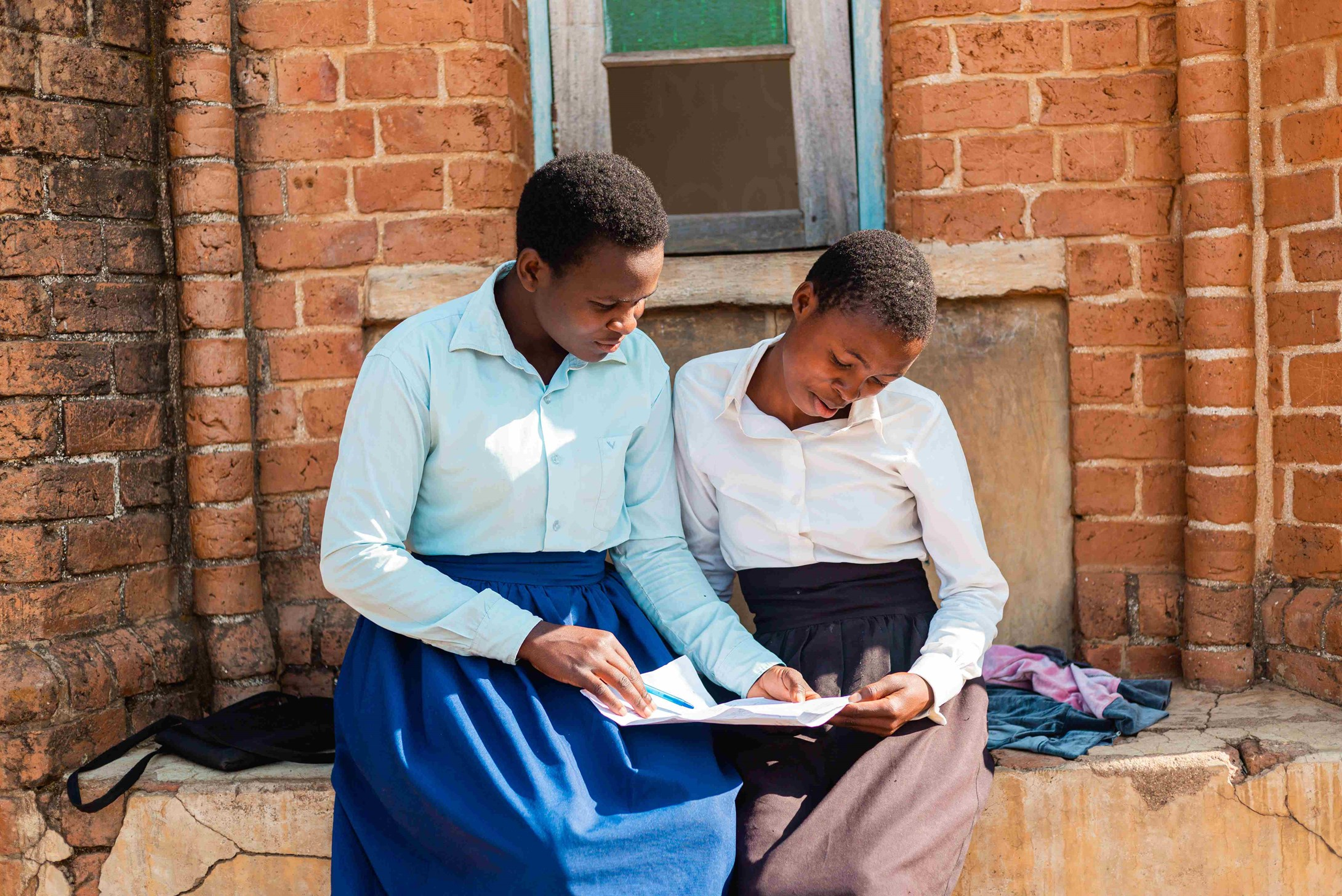 Two girls from Malawi sitting next to each other and reading together.